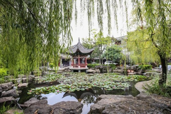 A traditional pavilion over a pond with lily pads, surrounded by rocks and willow trees. - Chuxiong Yuyu Holiday Hotel (Chuxiong City)