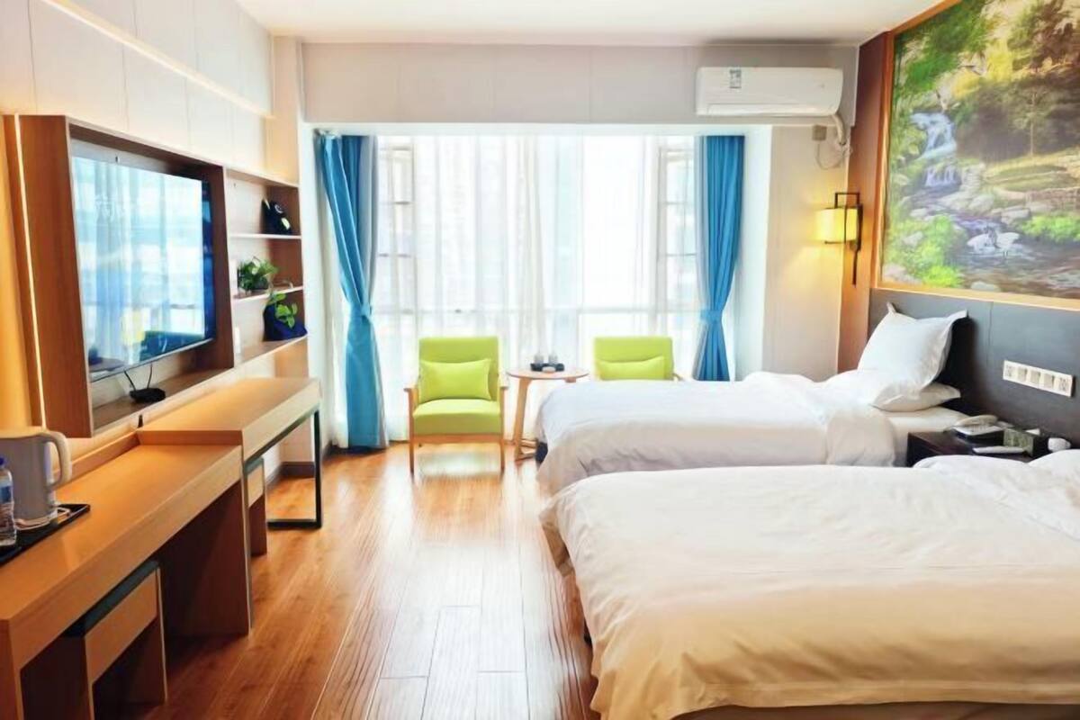 Une chambre d’hôtel avec deux lits, une télévision, un bureau avec une chaise, une petite table et un tableau au mur.