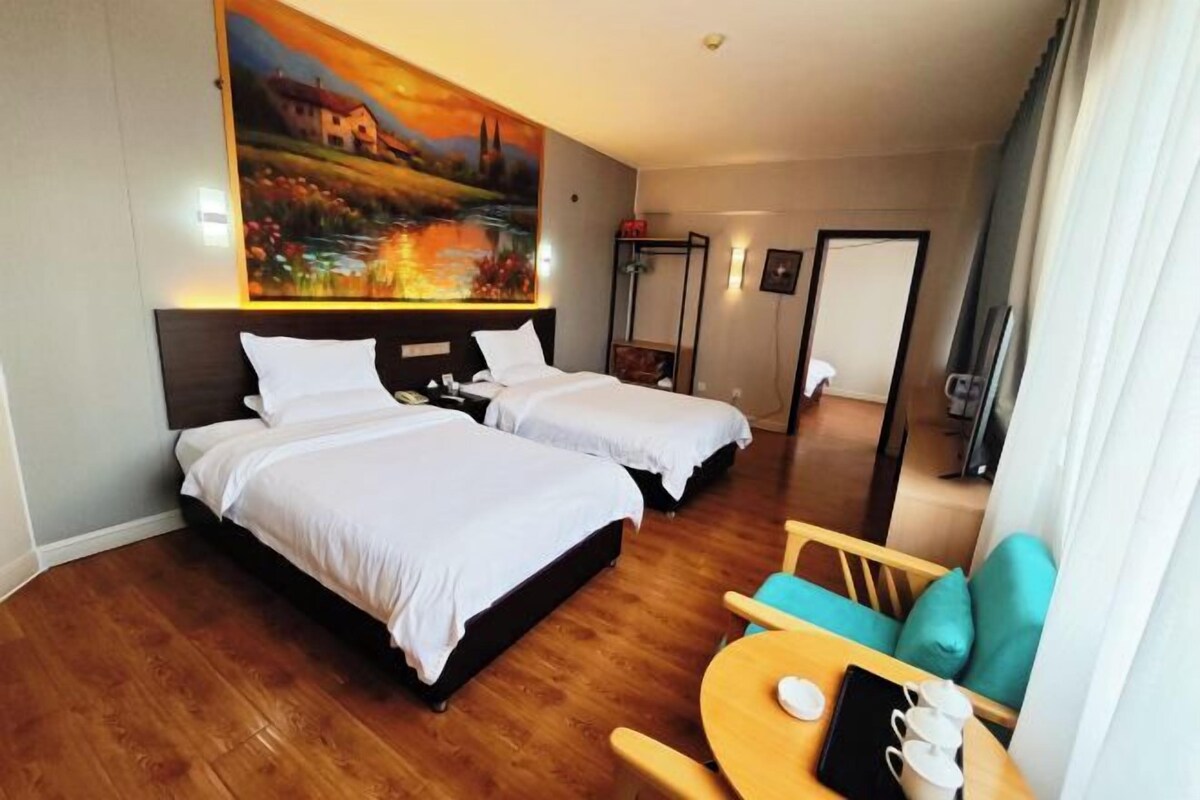 Habitación de hotel con dos camas, piso de madera, un cuadro en la pared, una mesita con tazas y una silla.