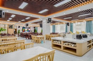 Uma sala de jantar ampla, com várias mesas e cadeiras, uma ilha central com pia e uma tela de televisão.