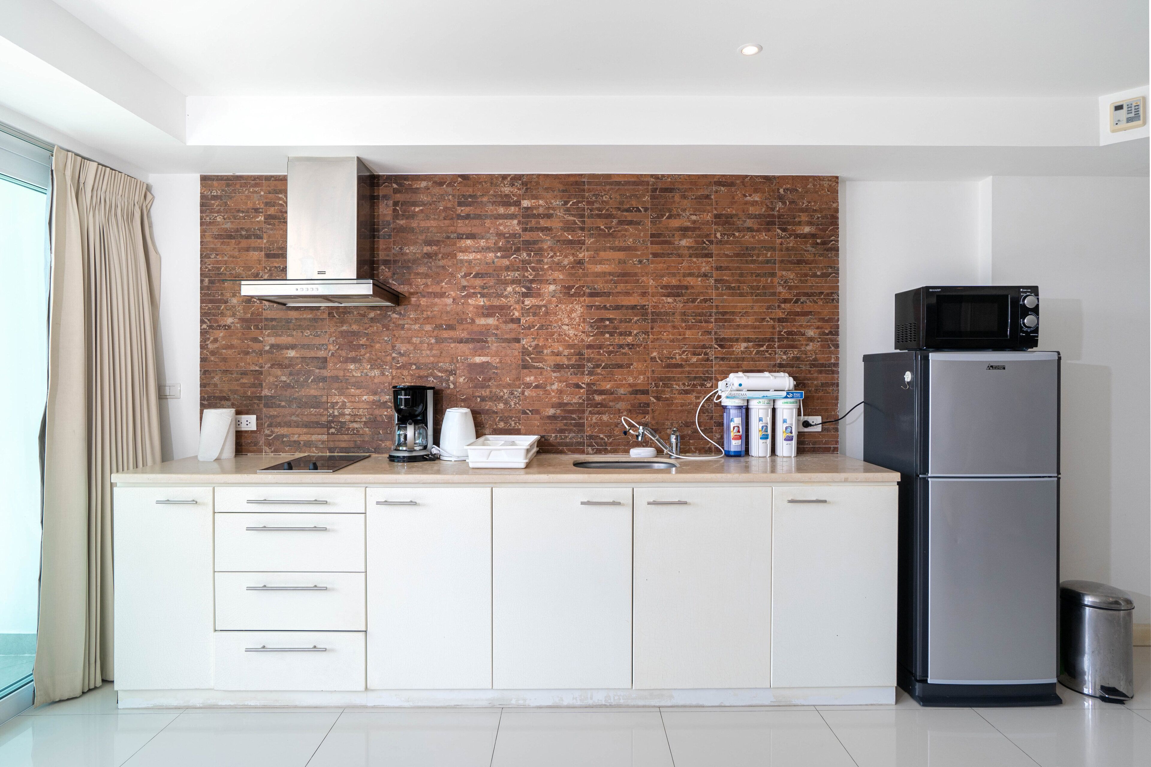 A modern kitchen with white cabinets, a brick backsplash, a stainless steel refrigerator, and a microwave.
