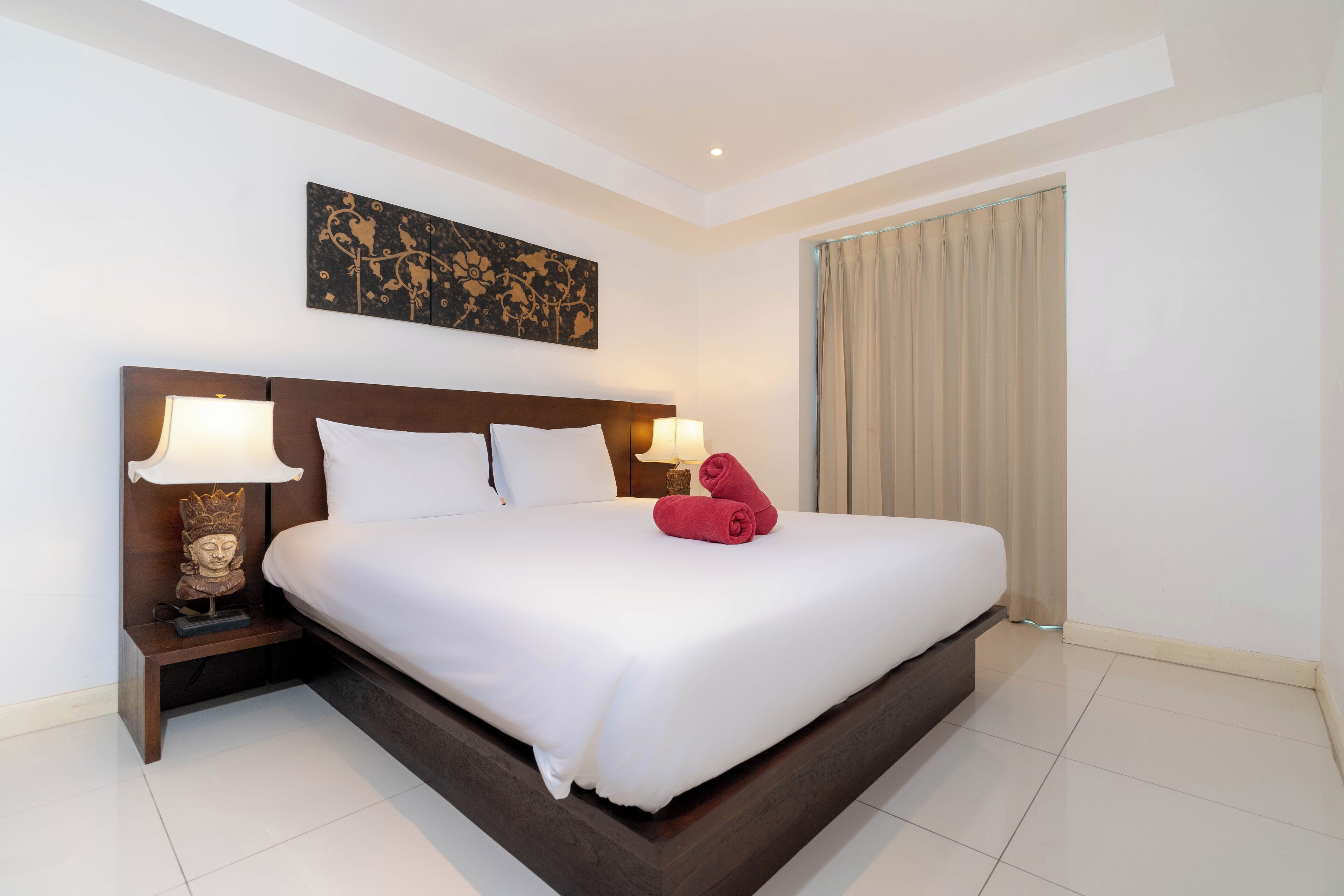 A large bed with white linens, two bedside lamps, a decorative headboard, and a wall-mounted artwork.