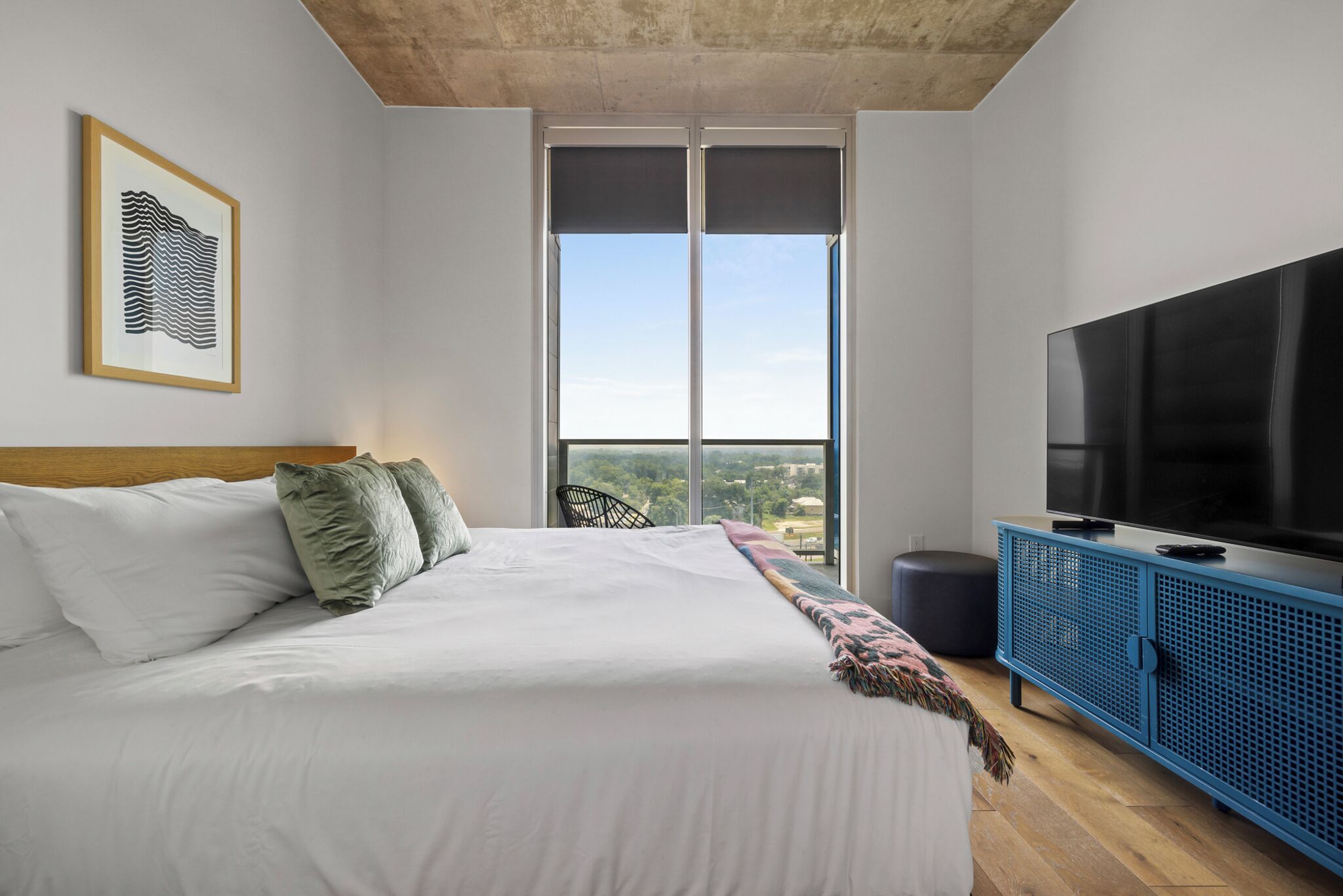 A modern bedroom with a large bed, a television, and a view of the city through large windows.