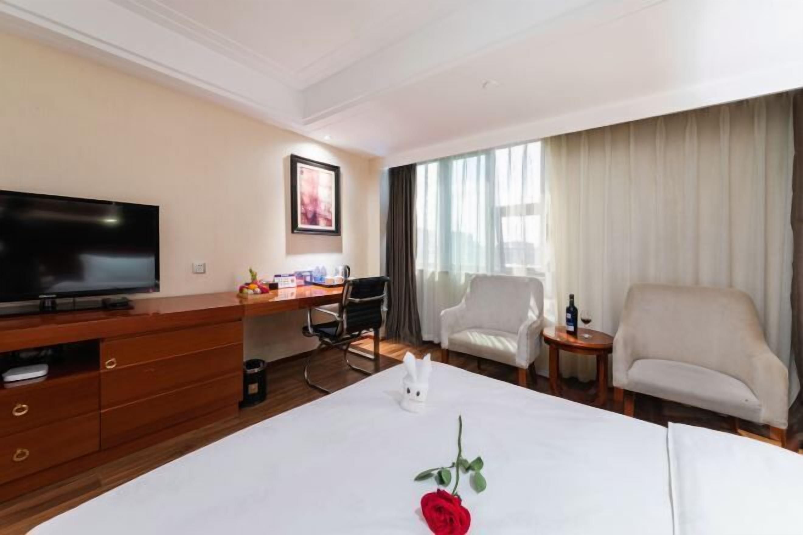 Een hotelkamer met een bed, een televisie, een bureau, twee stoelen en een raam met gordijnen.