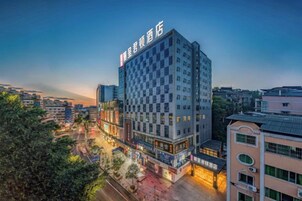 Un hotel de varios pisos con un letrero llamativo en la parte superior, rodeado de otros edificios y árboles.