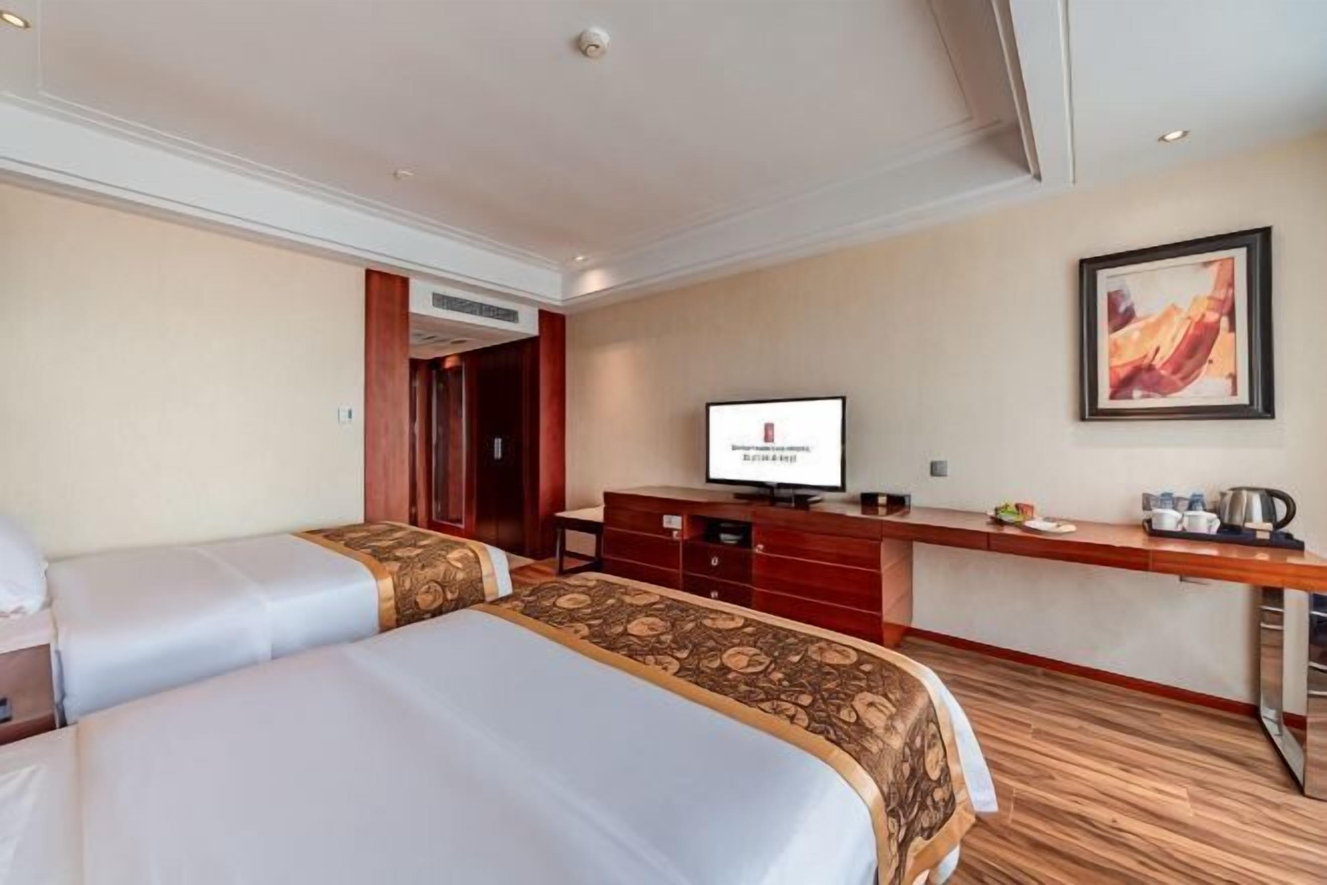 Une chambre d’hôtel avec deux lits, une télévision, un bureau et un tableau au mur.
