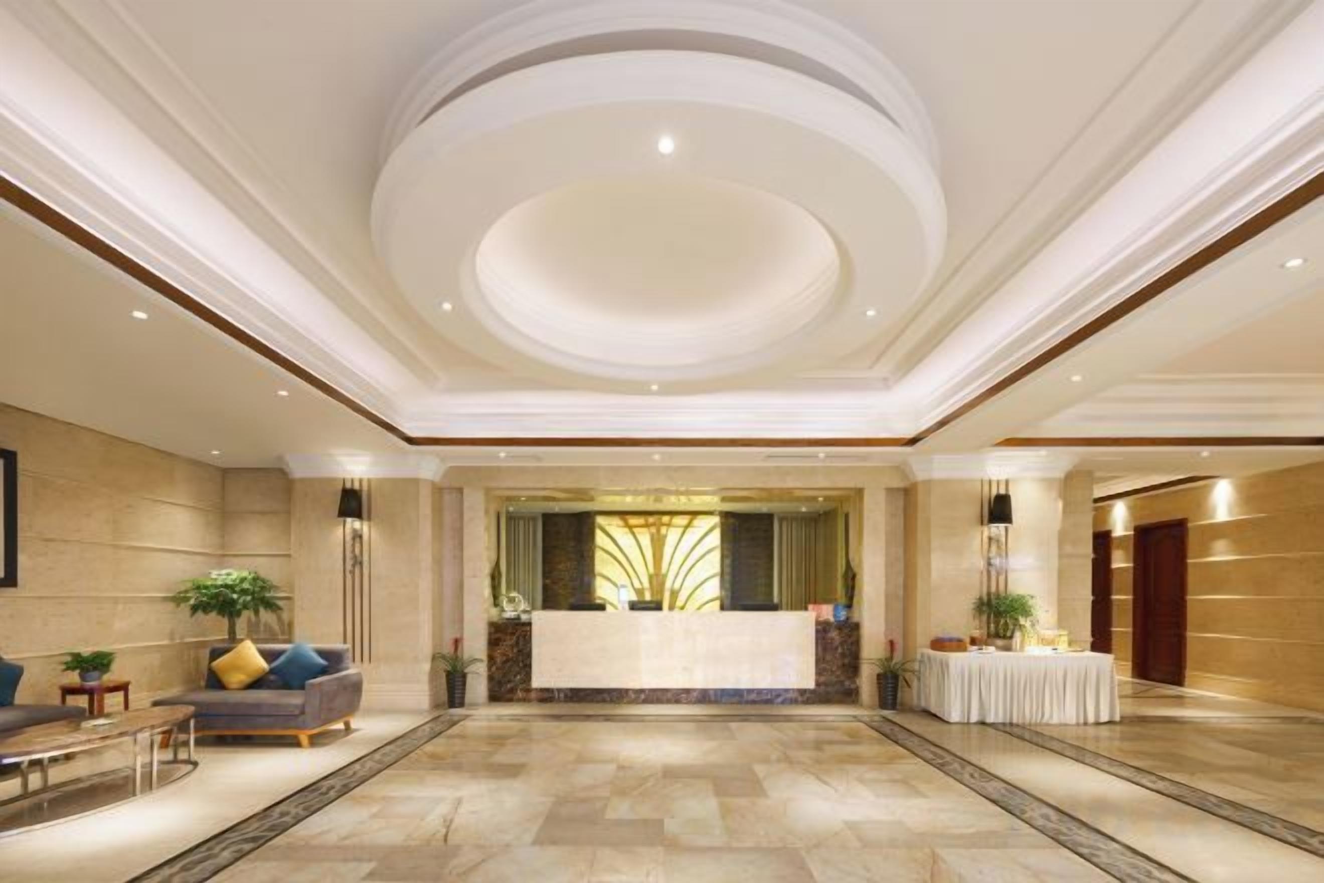 A spacious lobby with a reception desk, seating area, and a large chandelier.