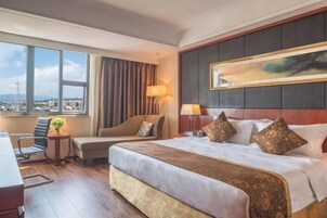 Habitación de hotel con una cama grande, un escritorio, una silla, vista a la ciudad y un cuadro en la pared.