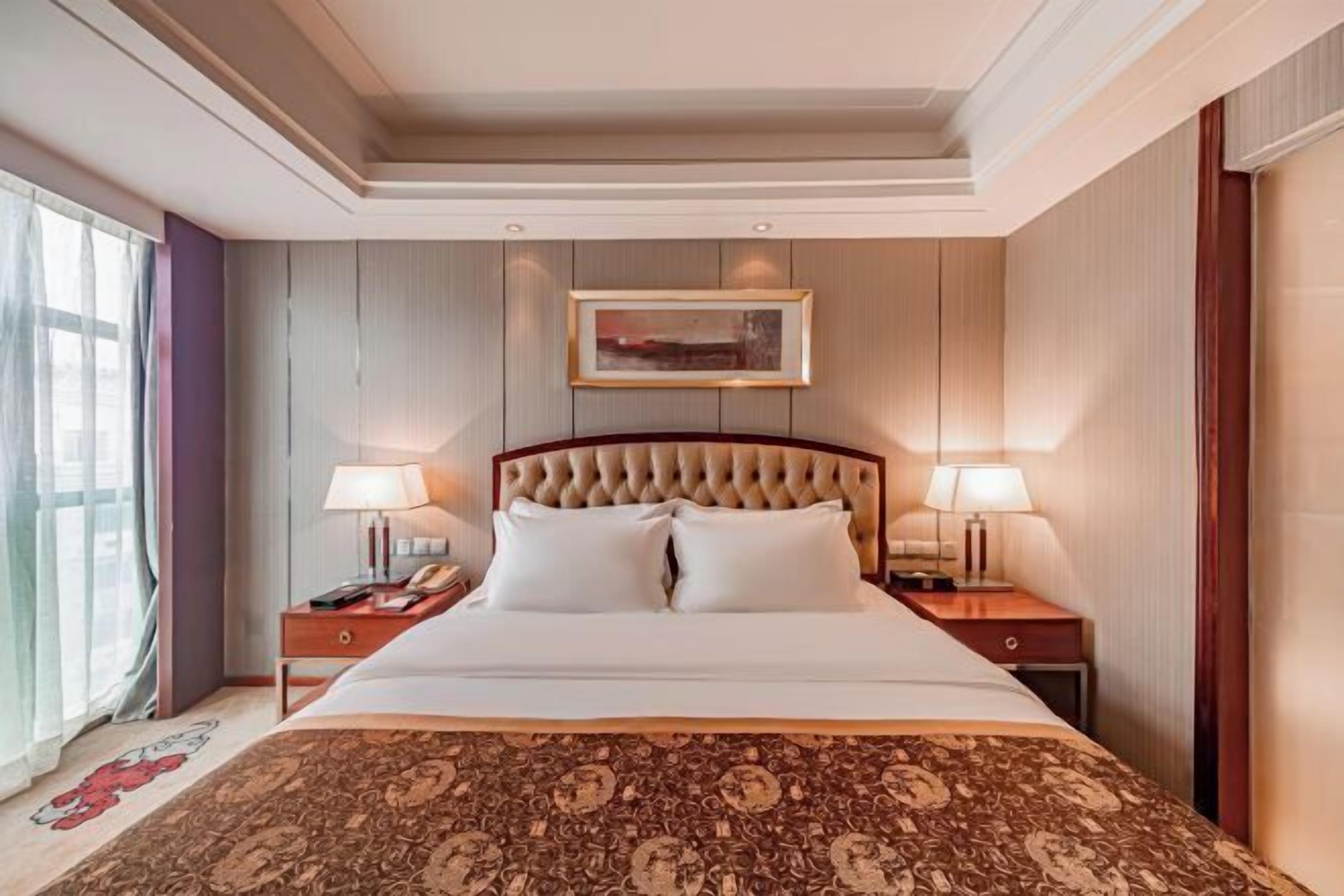 A hotel room with a large bed, two bedside tables with lamps, a framed picture on the wall, and a window with curtains.
