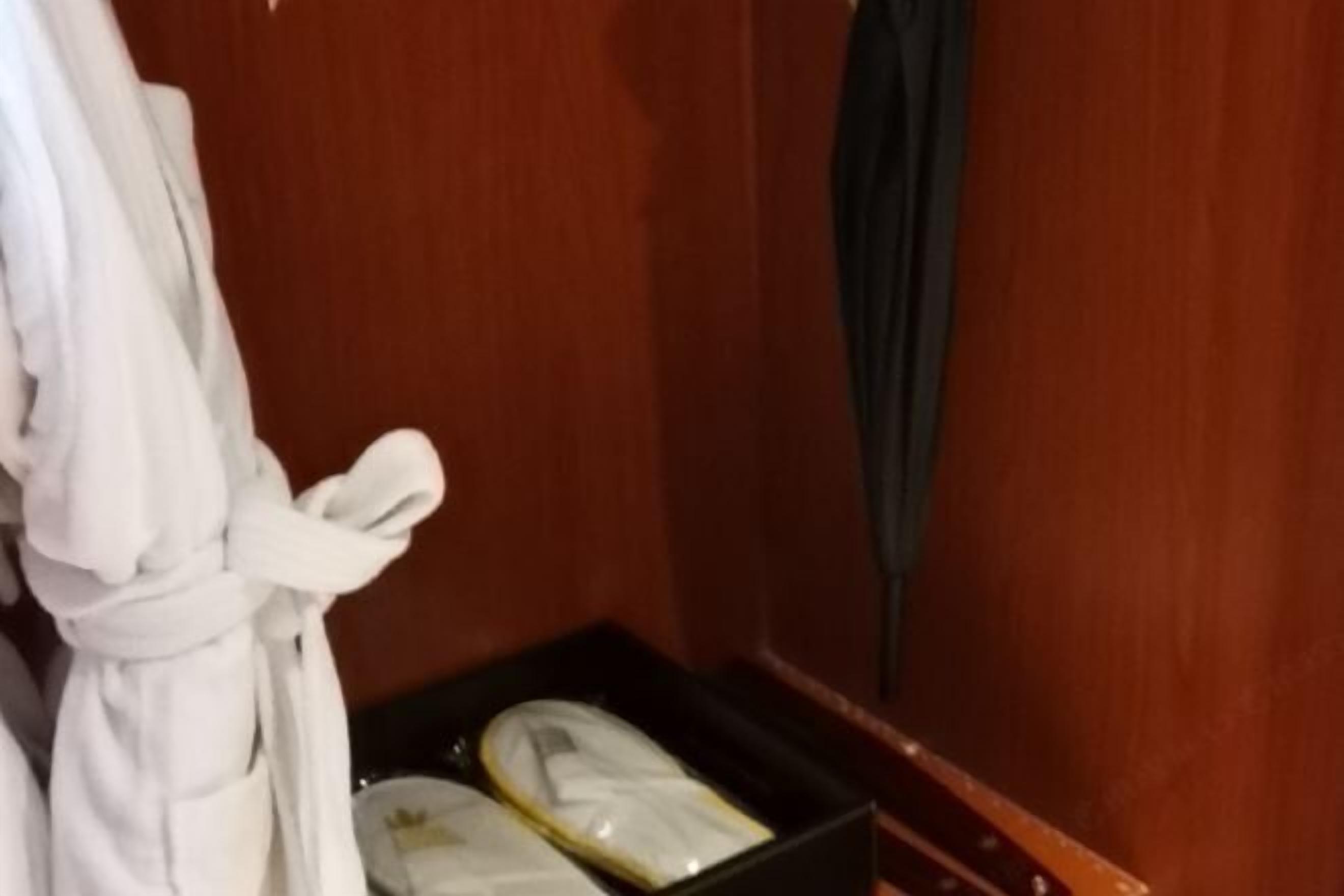 A wooden room with a white bathrobe hanging on a hook and a black box containing toiletries.