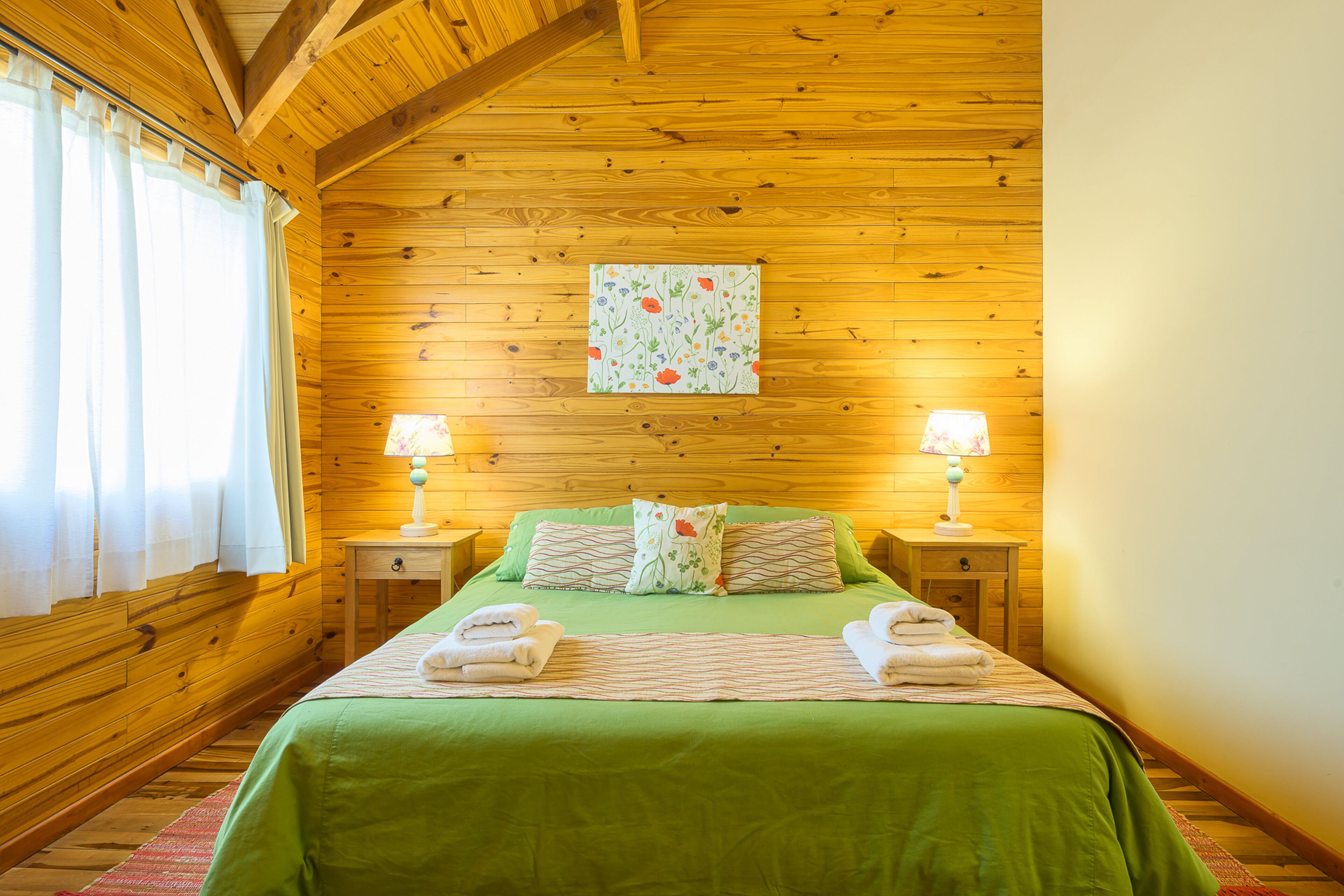 Ein Schlafzimmer mit Holzwänden, einem Bett, zwei Nachttischlampen und einem Fenster mit Vorhängen.
