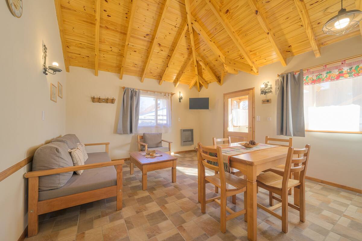 Ein gemütliches Zimmer mit Holzboden, einer Couch, einem Esstisch mit Stühlen und einem Fenster mit Vorhängen.