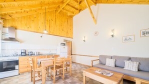 A kitchen with wooden cabinets, a dining table with chairs, a gray sofa, and a tiled floor. - Apartments Bariloche - San Martin de los Andes Lodge (San Martín de los Andes)
