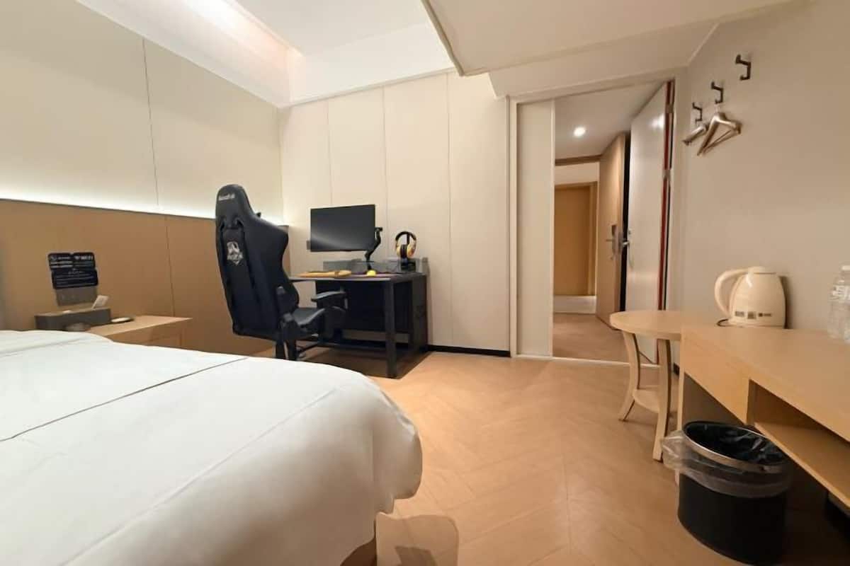 Een hotelkamer met een bed, bureau, computer en een prullenbak.