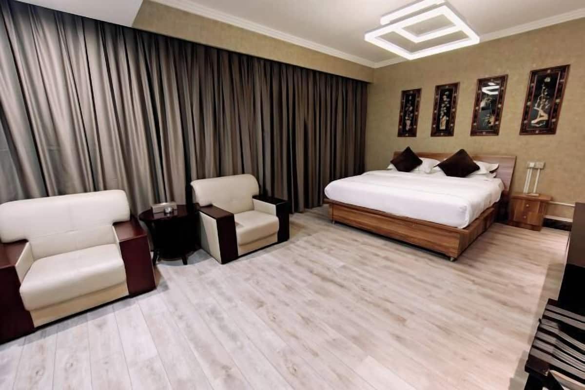 Een moderne hotelkamer met een groot bed, twee fauteuils, een klein tafeltje en een groot raam met gordijnen.