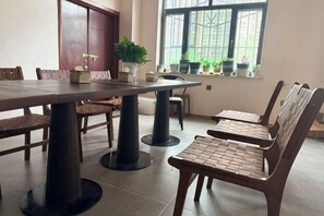 Een eetgedeelte met een lange tafel en stoelen, een potplant en een raam met planten op de vensterbank.