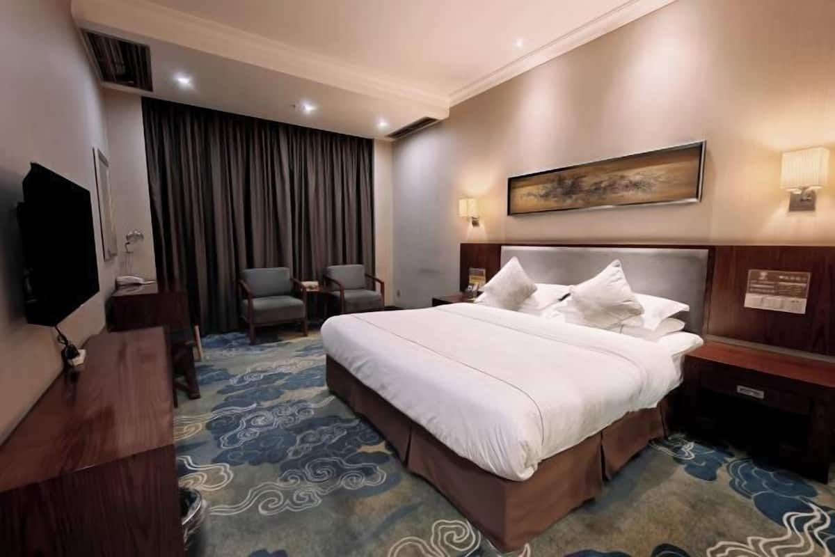 Een hotelkamer met een groot bed, een bureau, een stoel, een televisie en een schilderij aan de muur.