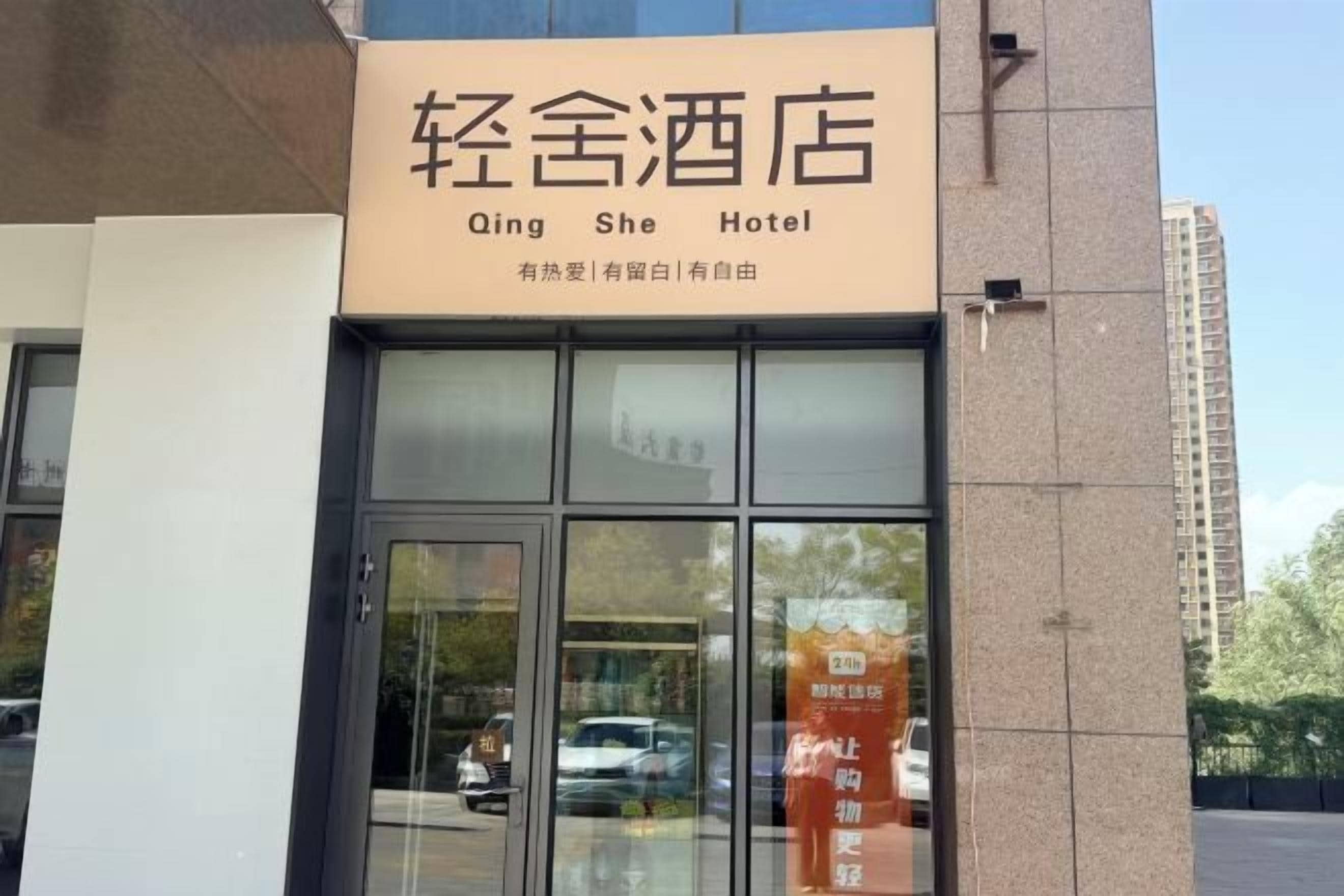 A hotel entrance with a sign reading 'Qing She Hotel' and a reflection of a car in the glass door.