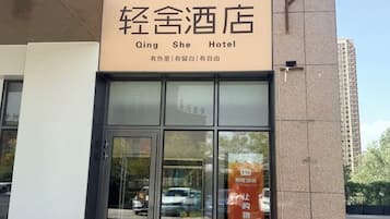 A hotel entrance with a sign reading 'Qing She Hotel' and a reflection of a car in the glass door.