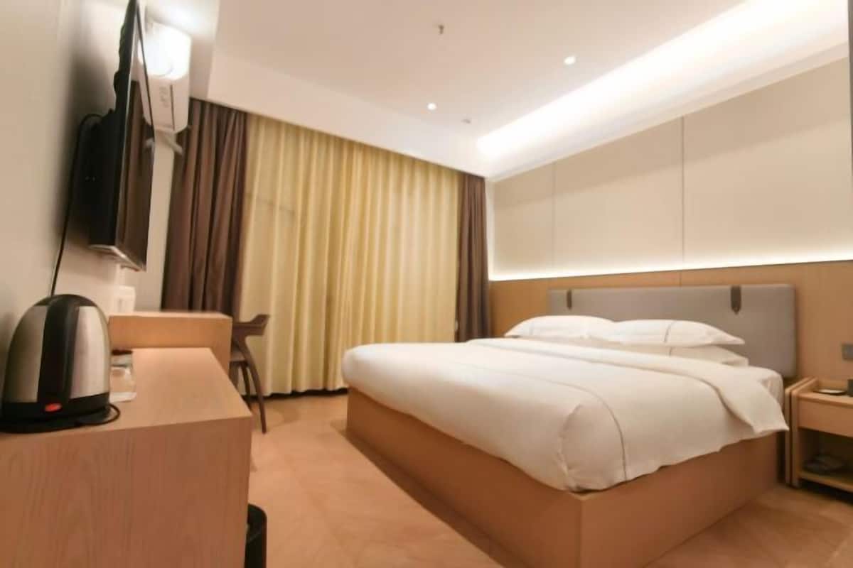 Een hotelkamer met een bed, een bureau met een waterkoker, een televisie en een gordijn.