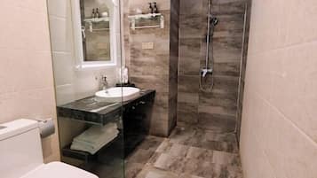 Een badkamer met een glazen wastafel, een douche en een marmeren vloer.