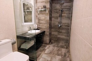Een badkamer met een glazen wastafel, een douche en een marmeren vloer.