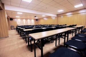 Un salón de conferencias con filas de mesas y sillas, un atril y suelo alfombrado.