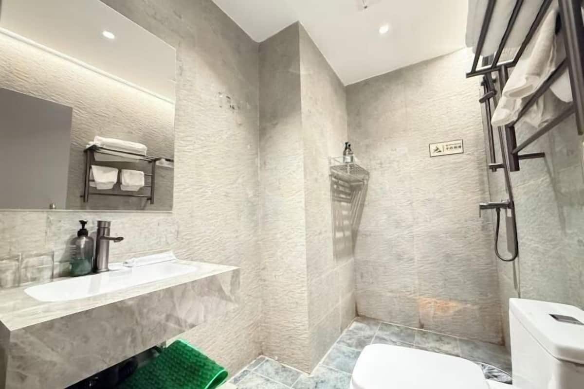 Een compacte badkamer met een marmeren wastafel, toilet, douche en handdoekhouder.