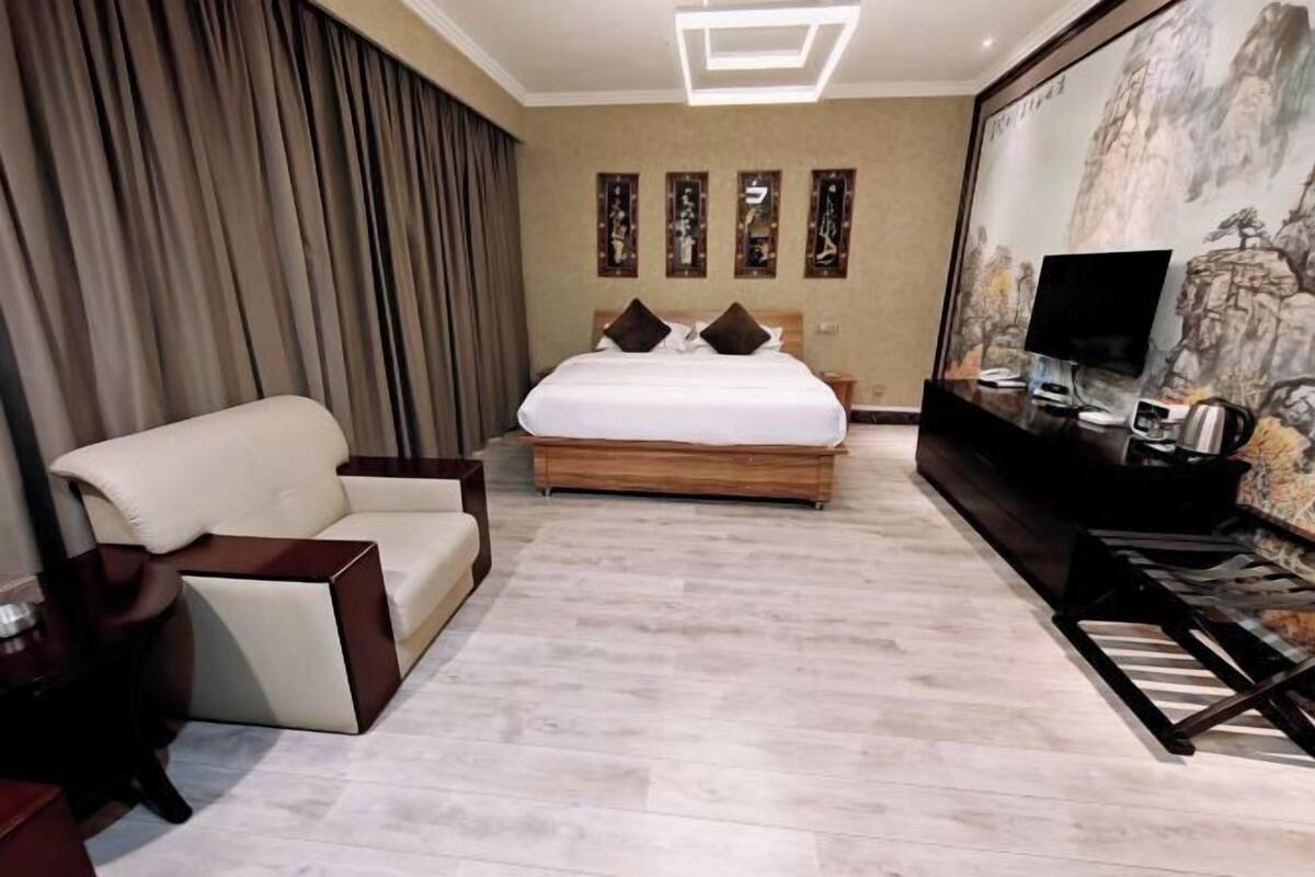 Une chambre d’hôtel avec un grand lit, une télévision, un bureau et un tableau au mur.