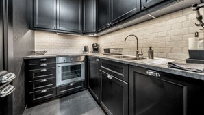A modern kitchen with dark cabinetry, a brick backsplash, and stainless steel appliances. - Warsaw Leszno Apartment with Parking - by Rentujemy (Warszawa)