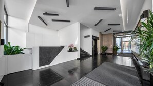 A modern lobby with a black marble reception desk, a staircase, and potted plants. - Warsaw Leszno Apartment with Parking - by Rentujemy (Warszawa)