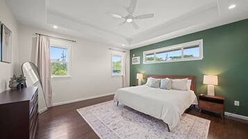 A bedroom with a bed, nightstands, a ceiling fan, and a view of greenery outside.