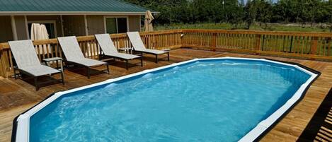 A rectangular above-ground pool with a wooden deck and lounge chairs.