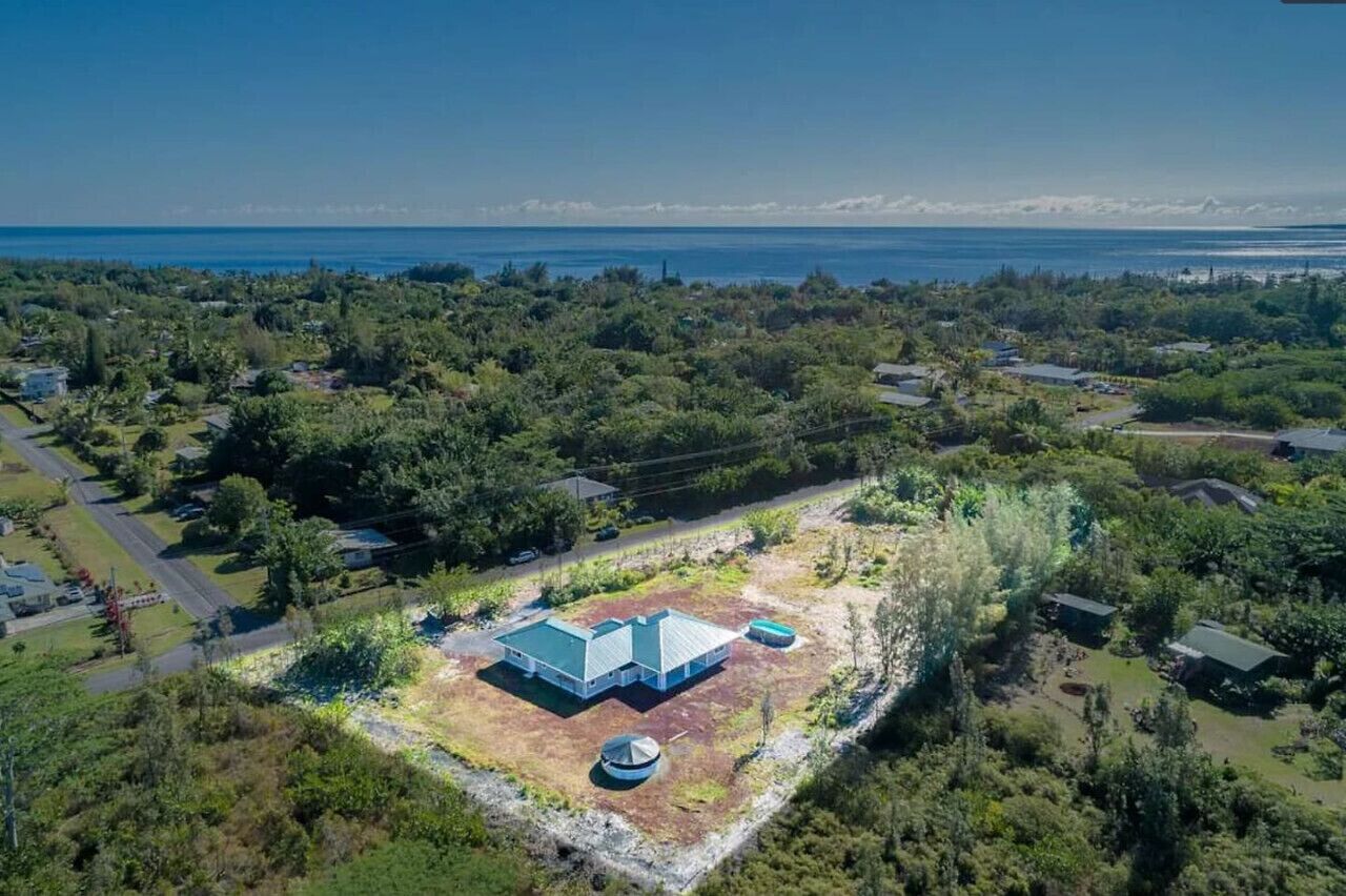 Une vue aérienne d’un quartier résidentiel, avec une grande maison dotée d’un toit végétalisé, entourée d’une végétation luxuriante et offrant une vue dégagée sur l’océan.