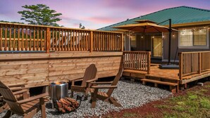 A wooden deck with Adirondack chairs, a fire pit, and a covered outdoor area with string lights. - Gorgeous Gated Retreat Near Ocean w/ Pool, Deck, Firepit on 1+ acre! (Keaau)