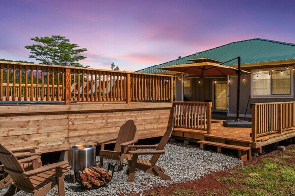 A wooden deck with Adirondack chairs, a fire pit, and a covered outdoor area with string lights.