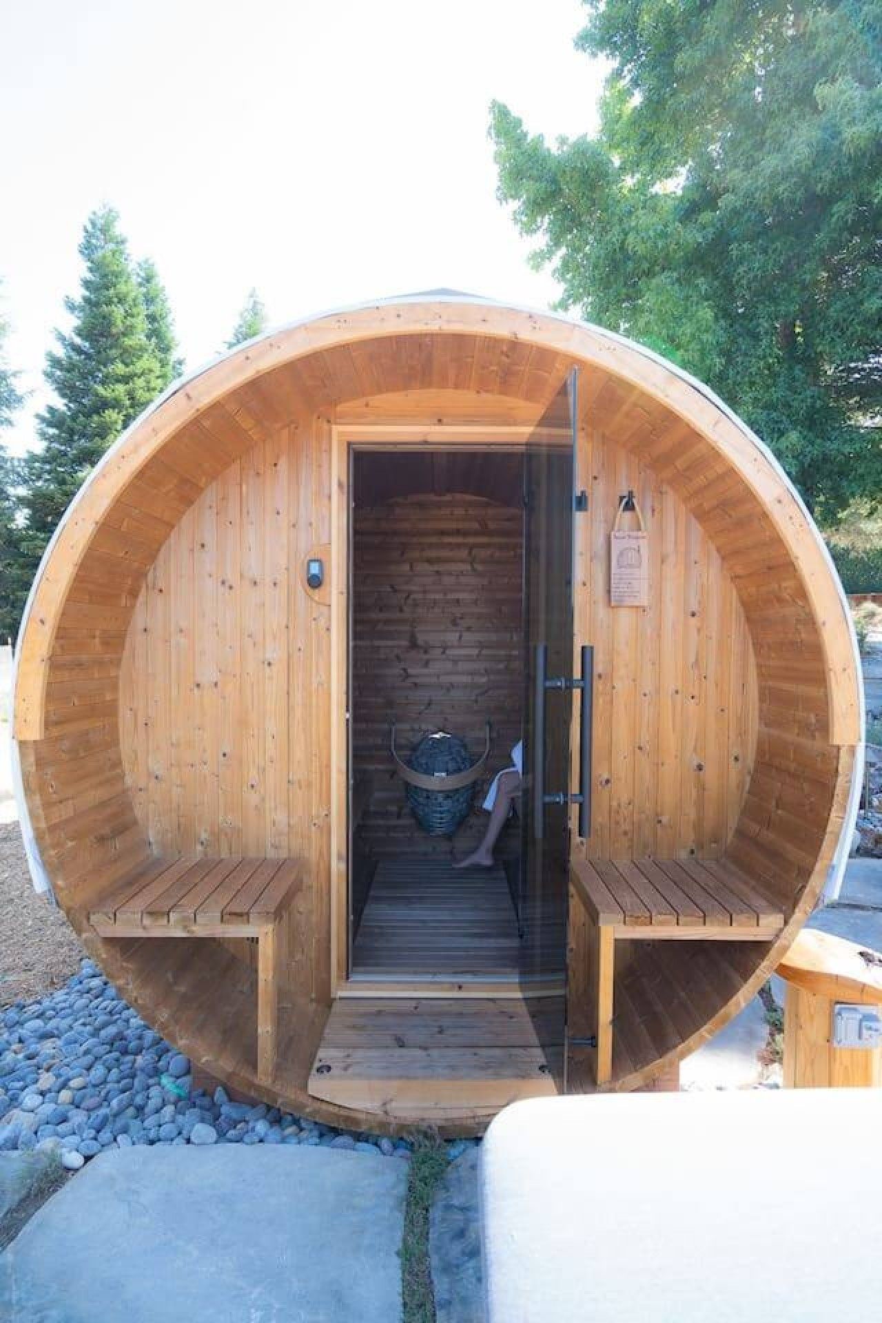 A wooden sauna with a bench inside, a door, and a small basket.