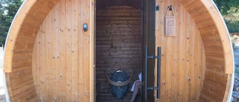 A wooden sauna with a bench inside, a door, and a small basket.