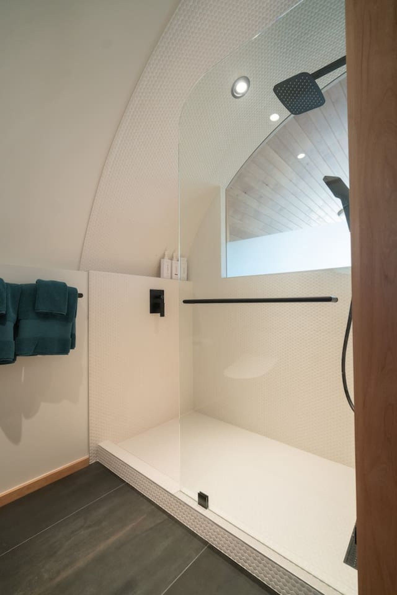 Eine moderne Dusche mit Glasabtrennung, einem Handtuchhalter mit gefalteten Handtüchern und einem Holzboden.
