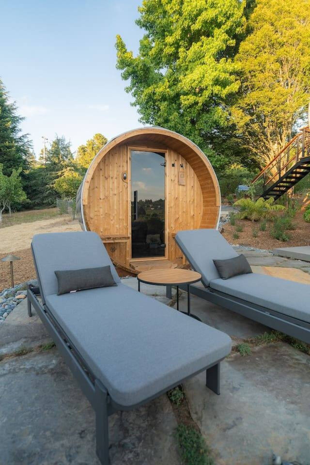 Een houten hutje met een ronde deur, twee comfortabele stoelen en een kleine tafel.