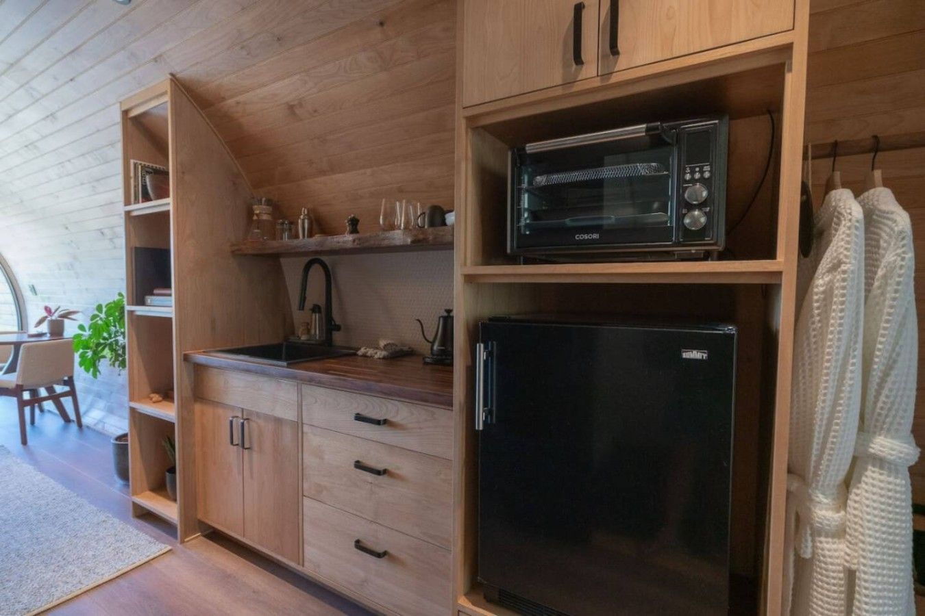 Une cuisine compacte avec des meubles de rangement en bois, un réfrigérateur noir, un four à micro-ondes et un évier.