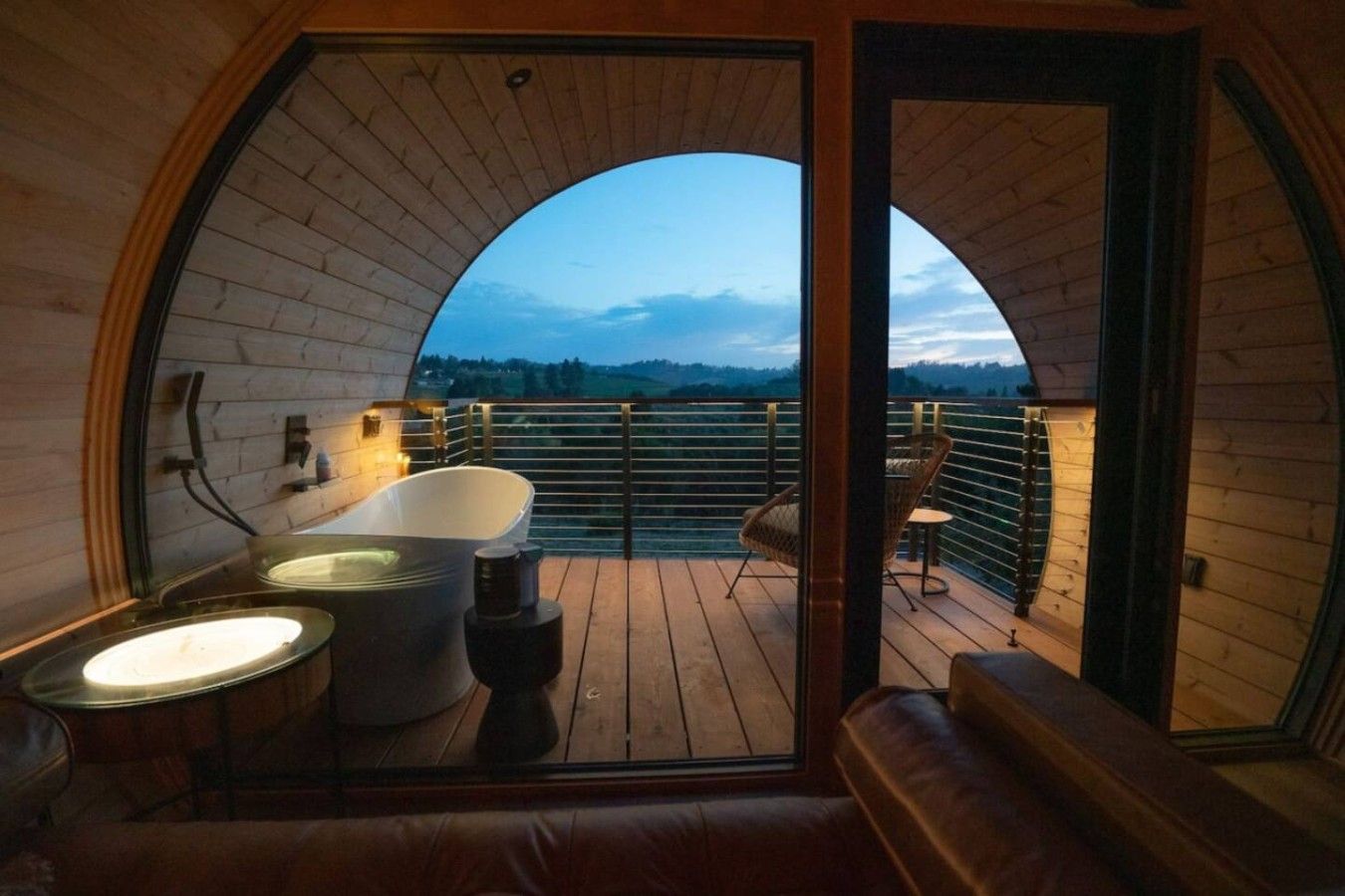 Un intérieur en bois avec une baignoire, un coin salon et un balcon offrant une vue.