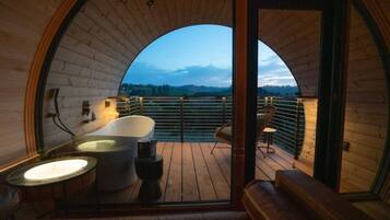 Un intérieur en bois avec une baignoire, un coin salon et un balcon offrant une vue.