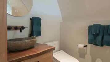 A bathroom with a wooden vanity, a round mirror, a toilet, and a towel rack.