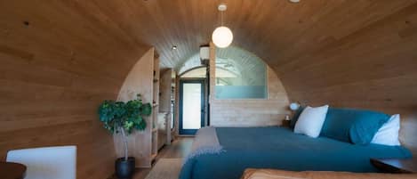 Une chambre mansardée chaleureuse avec un plafond cintré, un lit avec une literie bleue, une plante en pot et un petit coin salon.
