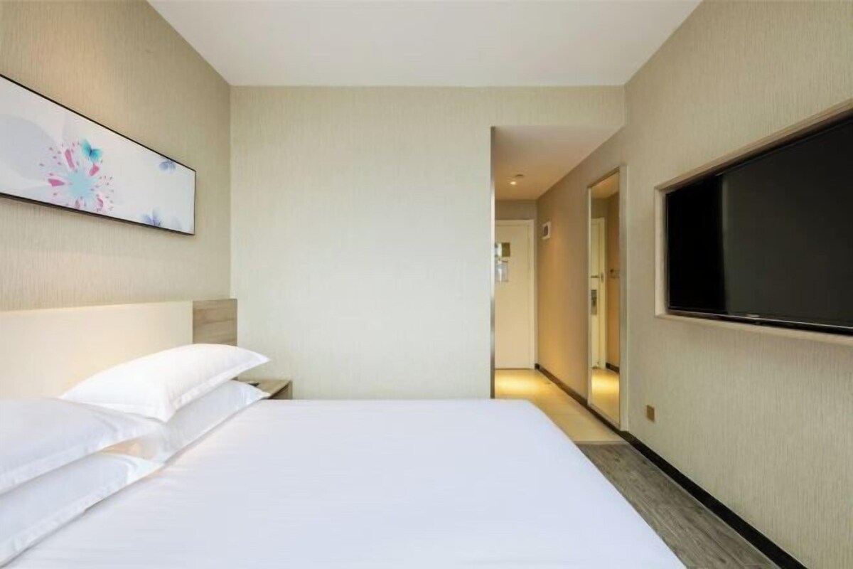 A hotel room with a bed, a flat-screen TV, and a painting on the wall.