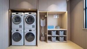 A laundry room with stacked washing machines and a shelving unit with storage bins. - HanTing Premium Hotel (Hangzhou Linping Intime City Subway Station) (Hangzhou)