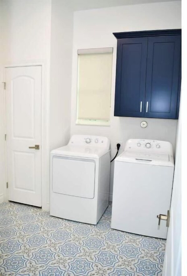 Un lavadero con dos lavadoras blancas, una puerta blanca y un armario azul.