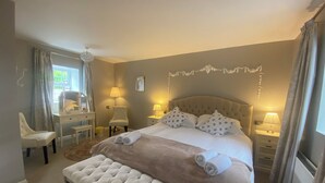 A bedroom with a large bed, two bedside tables with lamps, a desk with a chair, and a bench. - Ballyscullion Park Courtyard Cottages (Magherafelt)