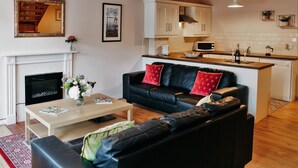 A modern living room with a fireplace, a black leather sofa, a wooden coffee table, and a television. - Ballyscullion Park Courtyard Cottages (Magherafelt)